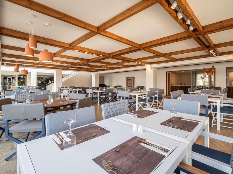 Jasna, nowoczesna restauracja z drewnianym sufitem z belkami i stylowo nakrytymi stołami.