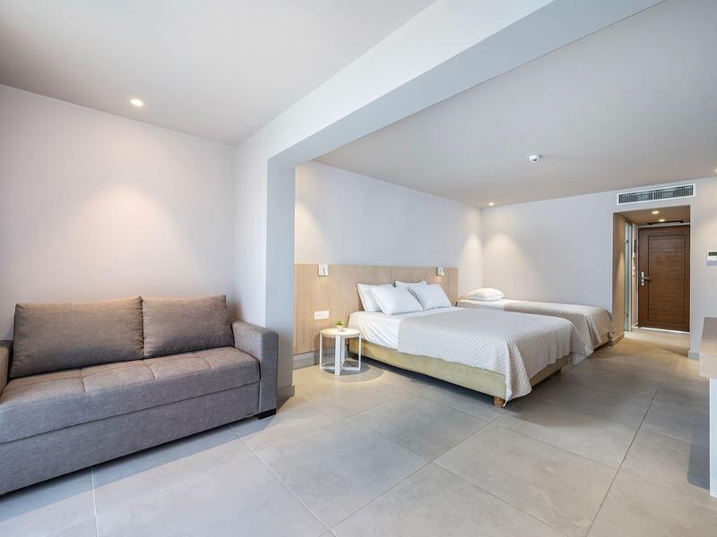 Jasny pokój hotelowy z łóżkiem podwójnym, sofą i nowoczesnym minimalistycznym wystrojem.