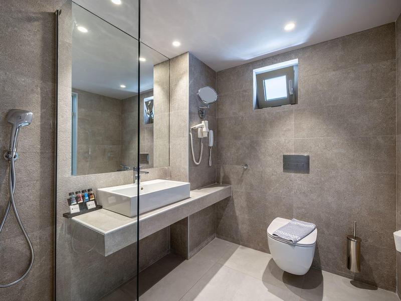 Nowoczesna łazienka hotelowa z prysznicem bez brodzika, umywalką i toaletą w neutralnych kolorach.