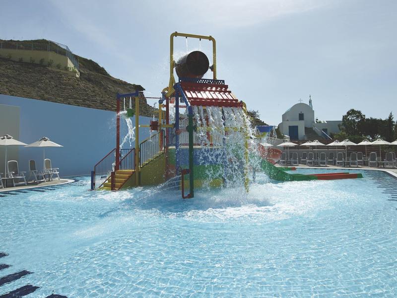 Kolorowa konstrukcja do zabaw wodnych z wiadrem i zjeżdżalniami w zewnętrznym basenie ośrodka wypoczynkowego.