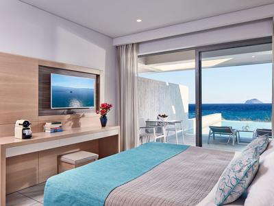 Nowoczesny pokój hotelowy z widokiem na morze, podwójne łóżko, biurko i taras z miejscem do siedzenia.