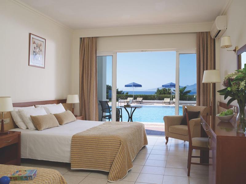 Jasny pokój hotelowy z łóżkiem podwójnym i widokiem na basen i morze.
