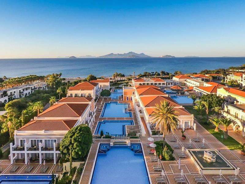 Widok z lotu ptaka na ośrodek z basenami, palmami i morzem w tle o wschodzie słońca.