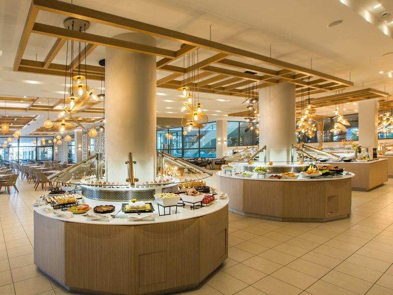 Duży obszar bufetu z owalnymi stanowiskami serwisowymi i nowoczesnym oświetleniem w jasnej restauracji.