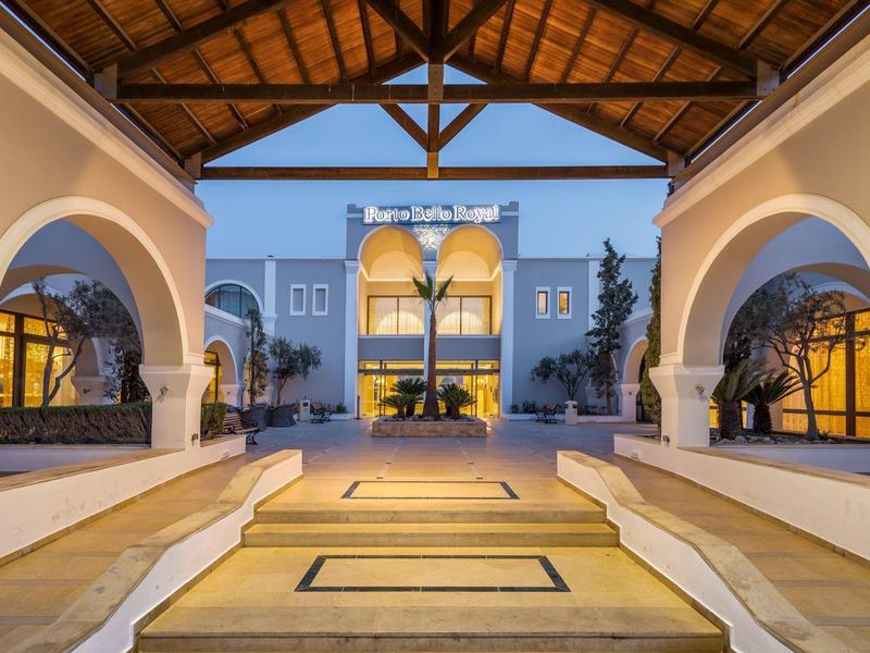 Wejście do hotelu z zadaszonym przejściem, schodami i symetryczną architekturą o zmierzchu.