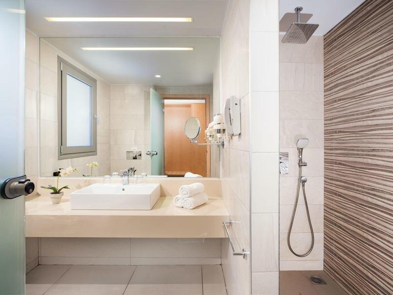 Jasna łazienka hotelowa z umywalką, dużym lustrem i oddzielnym prysznicem ze ścianą w drewniany wzór.