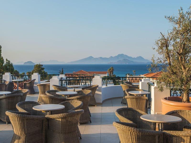 Taras na dachu z wiklinowymi fotelami i widokiem na morze oraz odległe wyspy pod czystym niebem.