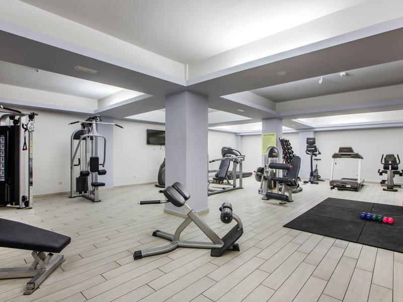 Jasno oświetlona siłownia z różnymi urządzeniami do ćwiczeń i strefami treningowymi.