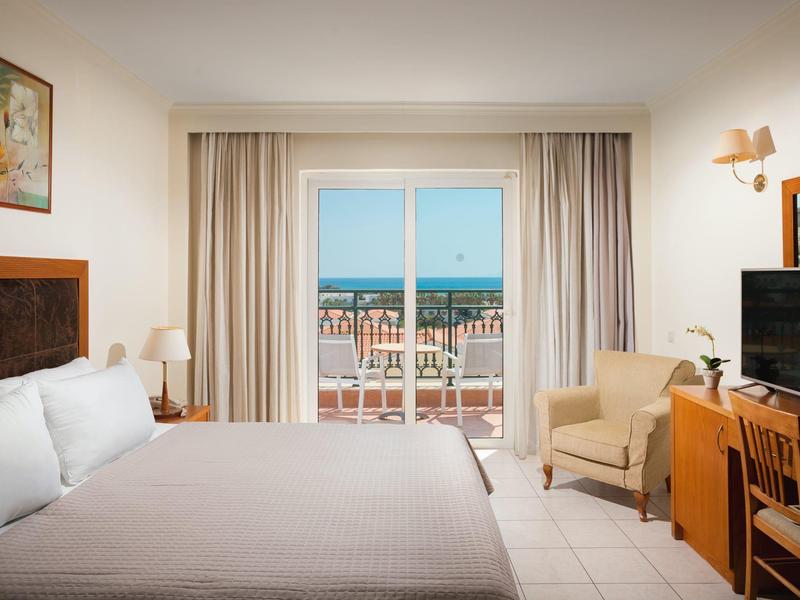 Jasny pokój hotelowy z łóżkiem, miejscem do siedzenia i balkonem z widokiem na morze.