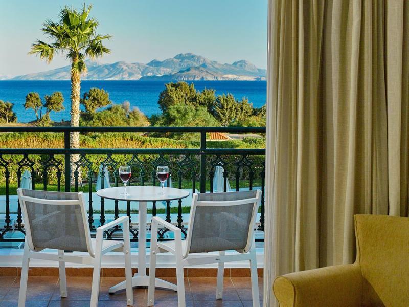 Balkon z stołem, dwoma krzesłami, widokiem na morze i zielony krajobraz w słoneczną pogodę.