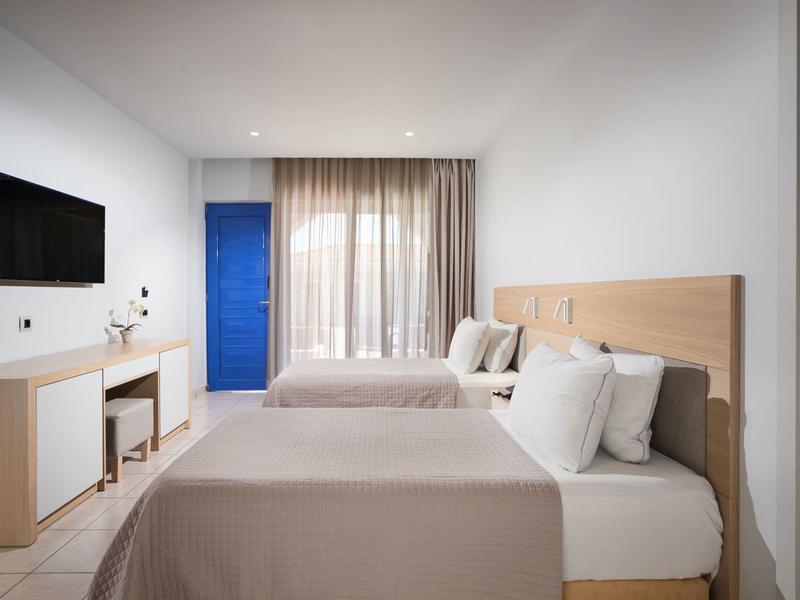 Nowoczesny pokój hotelowy z dwoma łóżkami, dużym oknem, zasłonami i telewizorem na ścianie.