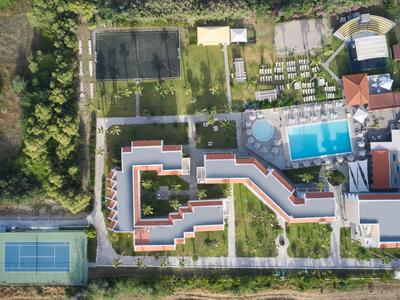 Luchtfoto van een hotel met twee zwembaden, een tennisbaan en omliggende groene gebieden.