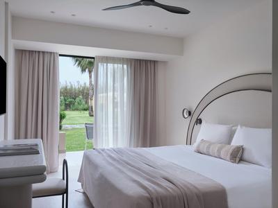 Modern hotelkamer met tweepersoonsbed, grijze beddengoed en uitzicht op tuin.