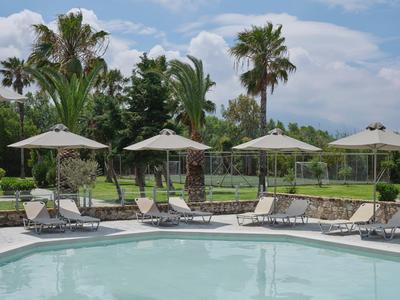 Een zwembad met ligstoelen en parasols in een tropische tuin bij bewolkte lucht.