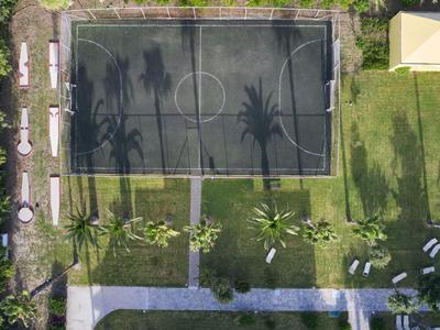 Luchtfoto van een voetbalveld met schaduwen van palmbomen en aangrenzend grasgebied.