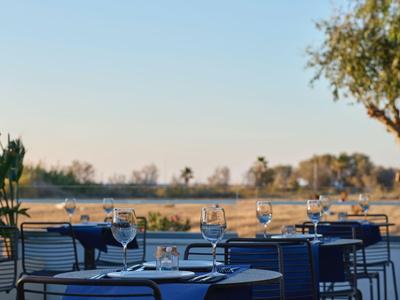 Außenrestaurant mit gedeckten Tischen und Blick auf einen ruhigen See bei Sonnenlicht.