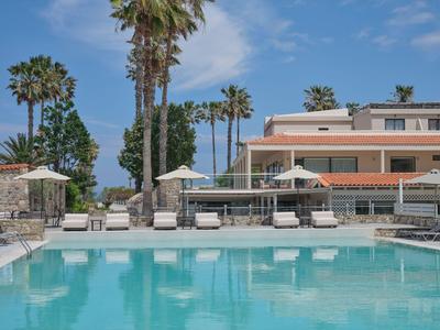 Hotel mit großem Pool und Sonnenschirmen, umgeben von Palmen unter blauem Himmel.