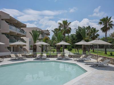 Poolbereich mit Liegestühlen und Sonnenschirmen neben einem Hotelgebäude und Palmen.