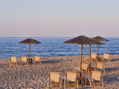 Sandstrand mit Liegestühlen und Sonnenschirmen am ruhigen Meer bei Sonnenuntergang.
