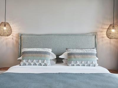 Modernes Doppelbett mit grauem Kopfteil, gemusterten Kissen und angehängten Korblampen.