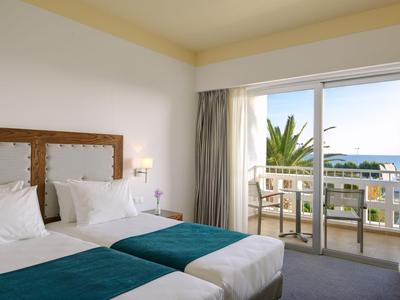 Hell eingerichtetes Hotelzimmer mit zwei Betten und Balkon mit Meerblick.