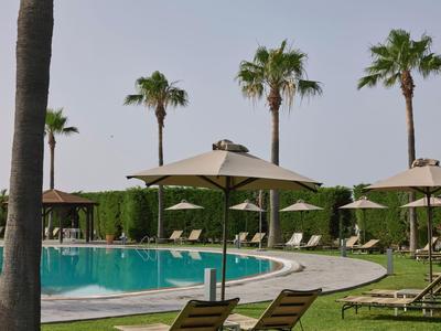 Runder Pool mit Sonnenschirmen, Liegestühlen und Palmen im Garten eines Hotels.