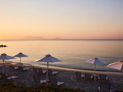 Strand mit Sonnenliegen und Sonnenschirmen bei ruhigem Meer im Sonnenuntergang.