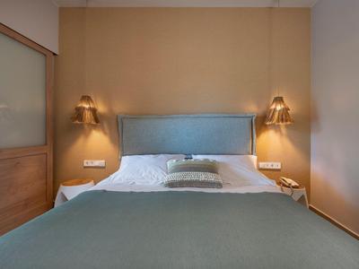 Schlicht eingerichtetes Hotelzimmer mit Doppelbett, Kissen und zwei Wandlampen.