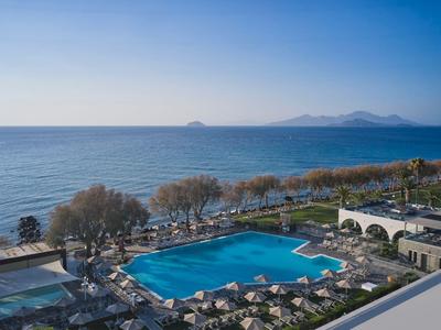 Hotel mit großem Pool an der Küste mit Blick auf das Meer und Berge im Hintergrund.