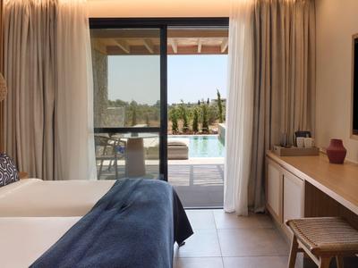 Hotelzimmer mit zwei Betten, Schreibtisch und Blick auf eine Terrasse mit Pool und Landschaft.