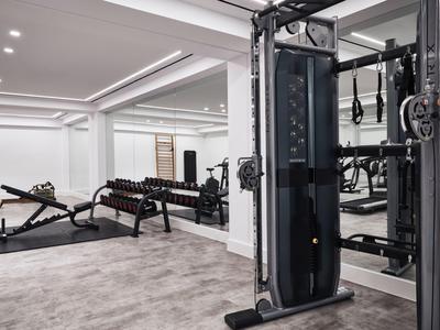 Moderner Hotel-Fitnessraum mit Hanteln, Trainingsgeräten und Spiegelwand.