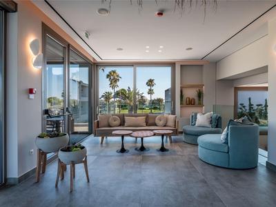 Moderne Hotellobby mit Sitzgelegenheiten, Glasfront und Ausblick auf Palmen bei Tageslicht.