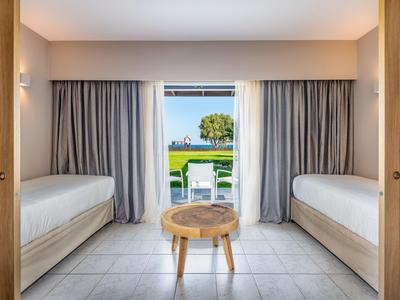 Moderner Hotelraum mit zwei Einzelbetten, Tisch und Blick auf Garten und Meer.
