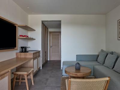 Moderner Hotelraum mit Sitzecke, Schreibtisch und Zugang zu einem dunklen Flur.