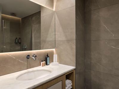 Helles Hotelbadezimmer mit zwei Waschbecken, großen Spiegeln und grauen Fliesen.