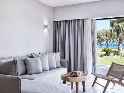 Helles Hotelzimmer mit grauem Sofa, Holztisch und Meerblick durch große Fenster.