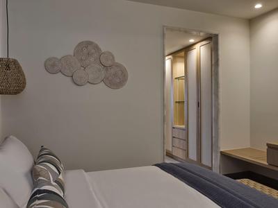 Modern eingerichtetes Hotelzimmer mit Bett, Wandkunst und Blick auf begehbaren Kleiderschrank.