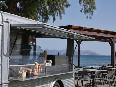 Moderner Food-Truck mit offener Theke neben Tischreihen am Strand mit Meerblick.