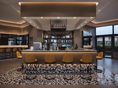 Moderner Hotelbarbereich mit gelben Stühlen und geometrischem Teppichmuster.