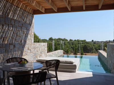 Überdachte Terrasse mit Stühlen und Tisch neben einem Pool mit Blick auf grüne Landschaft.