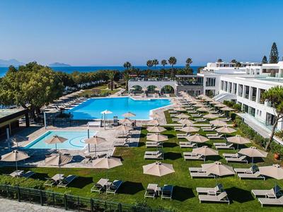 Großer Hotelpool mit Liegestühlen und Blick auf das Meer, umgeben von Palmen und grünen Rasenflächen.