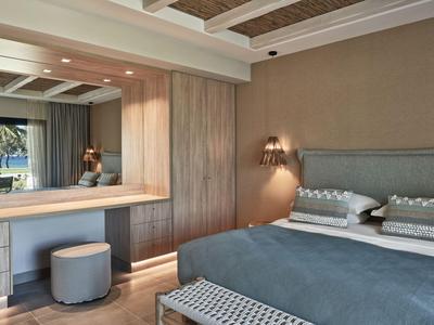 Modernes Hotelzimmer mit Doppelbett, großem Spiegel und Hocker vor Fenster mit Blick auf Palmen.