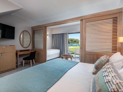 Modernes Hotelzimmer mit Doppelbett, Fernseher, Schreibtisch und Blick auf Terrasse und Garten.