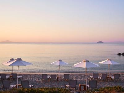 Strand mit Liegestühlen und Sonnenschirmen bei ruhigem Meer und Sonnenaufgang.