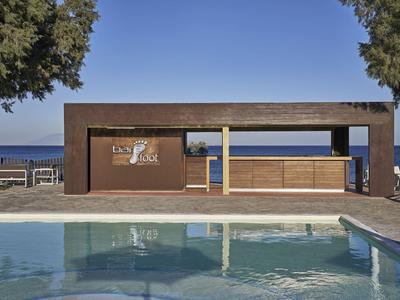 Moderner Poolbereich mit Holzbar, Sitzgelegenheiten und Blick auf das Meer.
