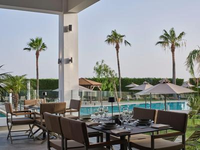 Moderner Außenbereich mit Tisch und Stühlen neben einem Pool und Palmen am Hotel.