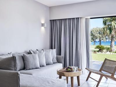 Helles Wohnzimmer mit grauem Sofa, Holztisch und Aussicht auf das Meer durch eine große Glastür.