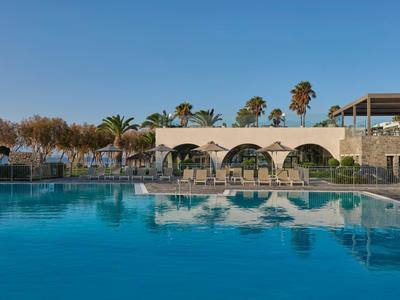 Großer Hotelpool mit klarem Wasser und Arkadenbau im Hintergrund unter blauem Himmel.
