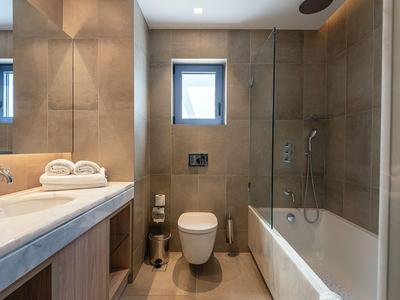 Modernes Badezimmer mit Dusche, Badewanne, Toilette und Waschbecken in neutralem Farbton.