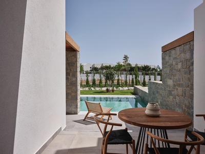 Moderner Hotelbalkon mit Holztisch, Stühlen und Blick auf den Pool bei klarem Himmel.